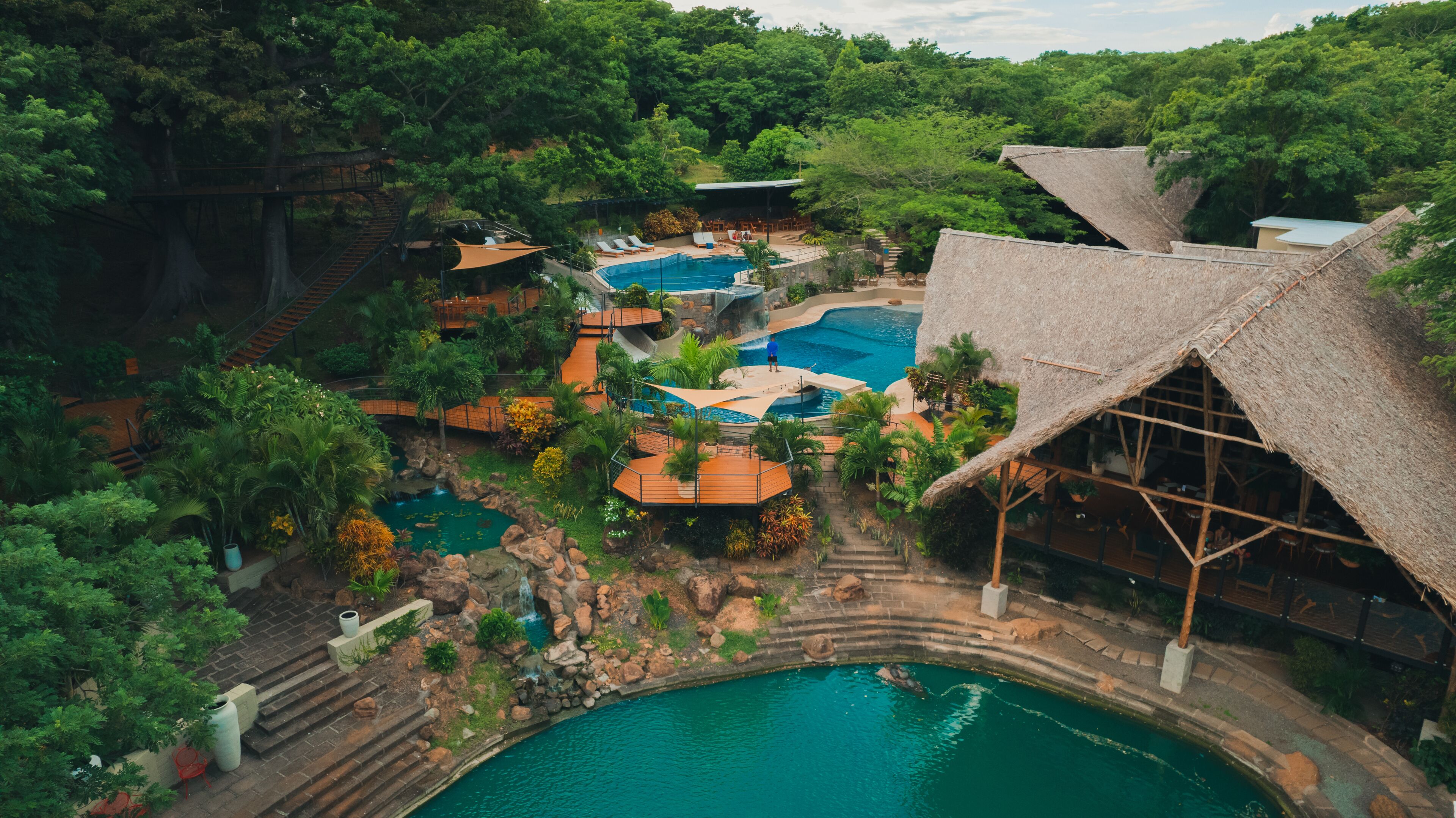 A resort with multiple swimming pools, a waterfall, and lush greenery.