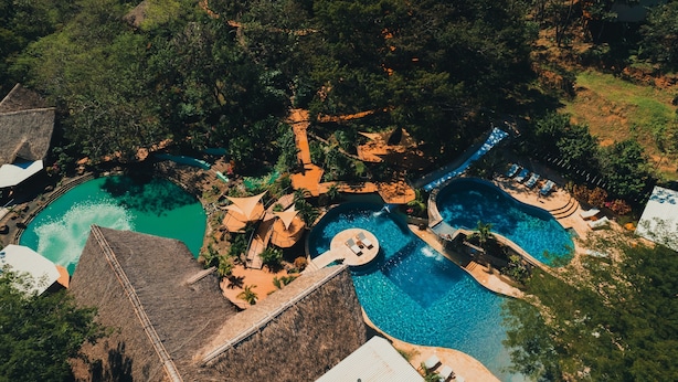 Vue aérienne d’un complexe hôtelier doté de plusieurs piscines, d’une cascade et d’une végétation luxuriante.