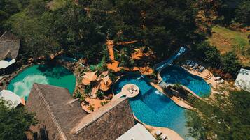 Escape to a tropical oasis with multiple pools surrounded by lush greenery and thatched-roof structures.