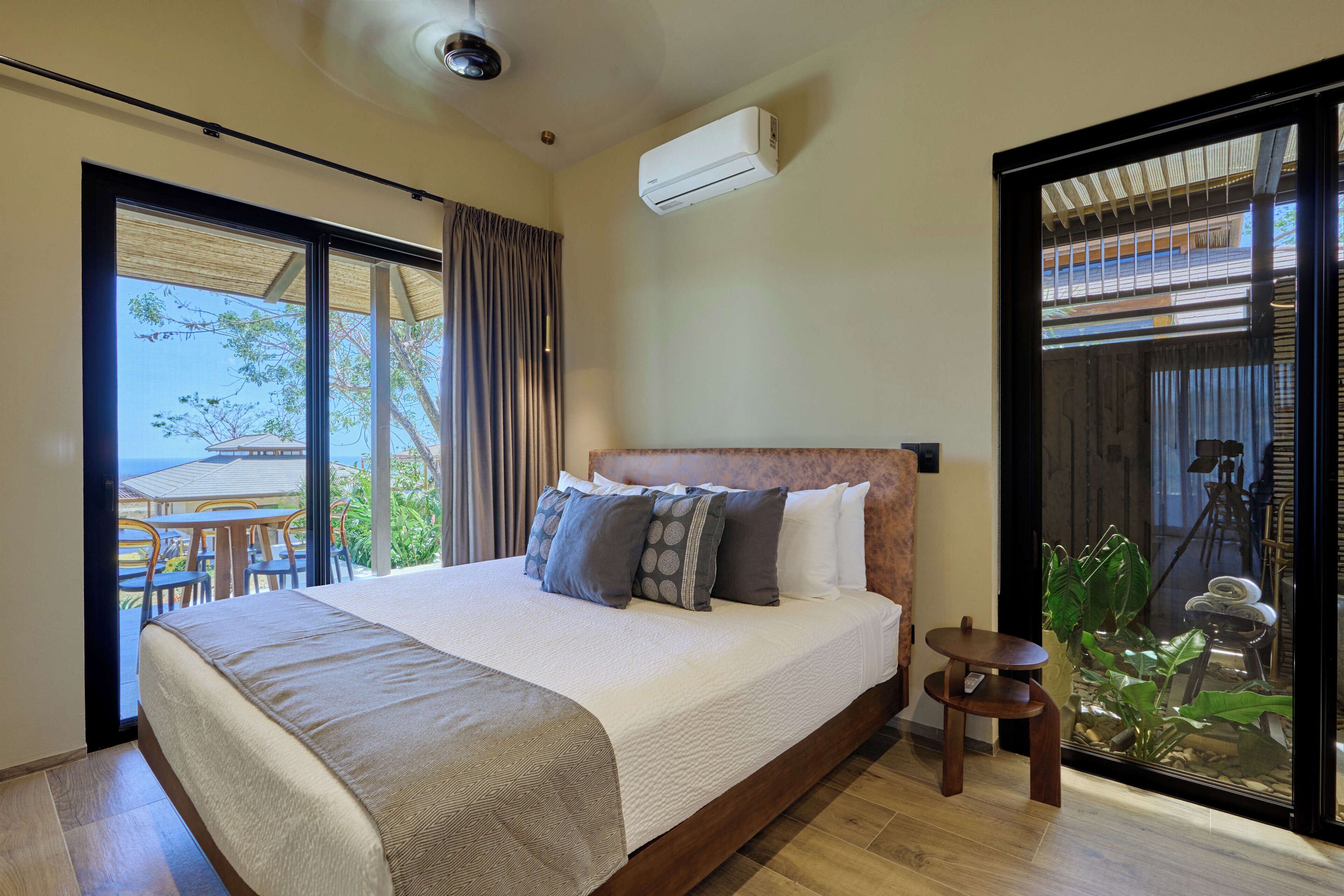 Una habitación de hotel moderna con una cama grande, una mesita pequeña y vistas al exterior.