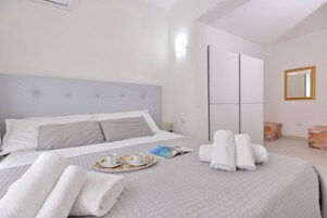 Una cama bien hecha con almohadas, una bandeja con tazas y un libro, y toallas enrolladas.