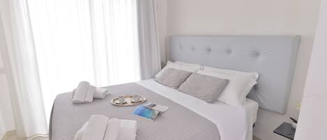 A neatly made bed with a quilted bedspread, a tray with cups and a book, and towels on the bed.