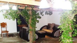 Una habitación rústica con un banco de madera, un sofá acolchado y una silla. Se aprecia una estructura de madera con hiedra colgando.