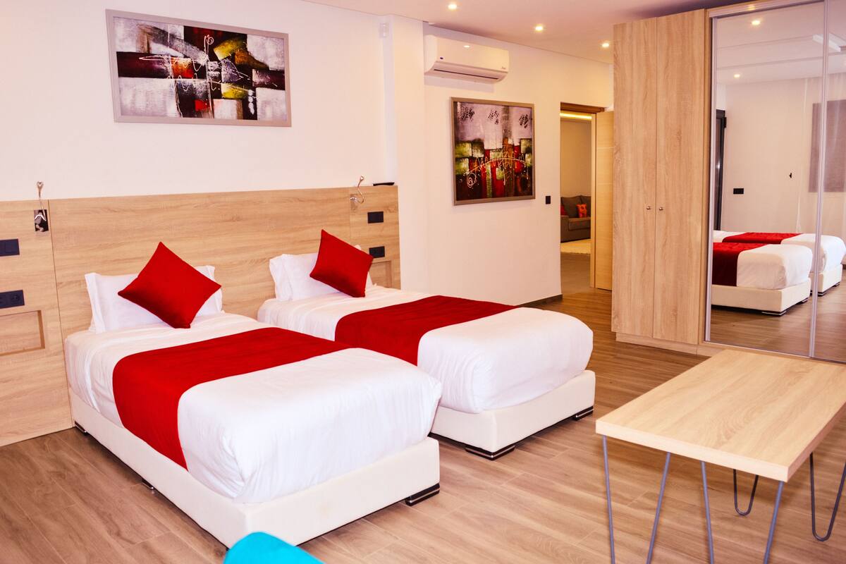 A hotel room with two beds, a wooden headboard, a small table, and artwork on the walls.