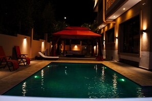 Une piscine surmontée d’un auvent rouge et bordée de chaises longues.
