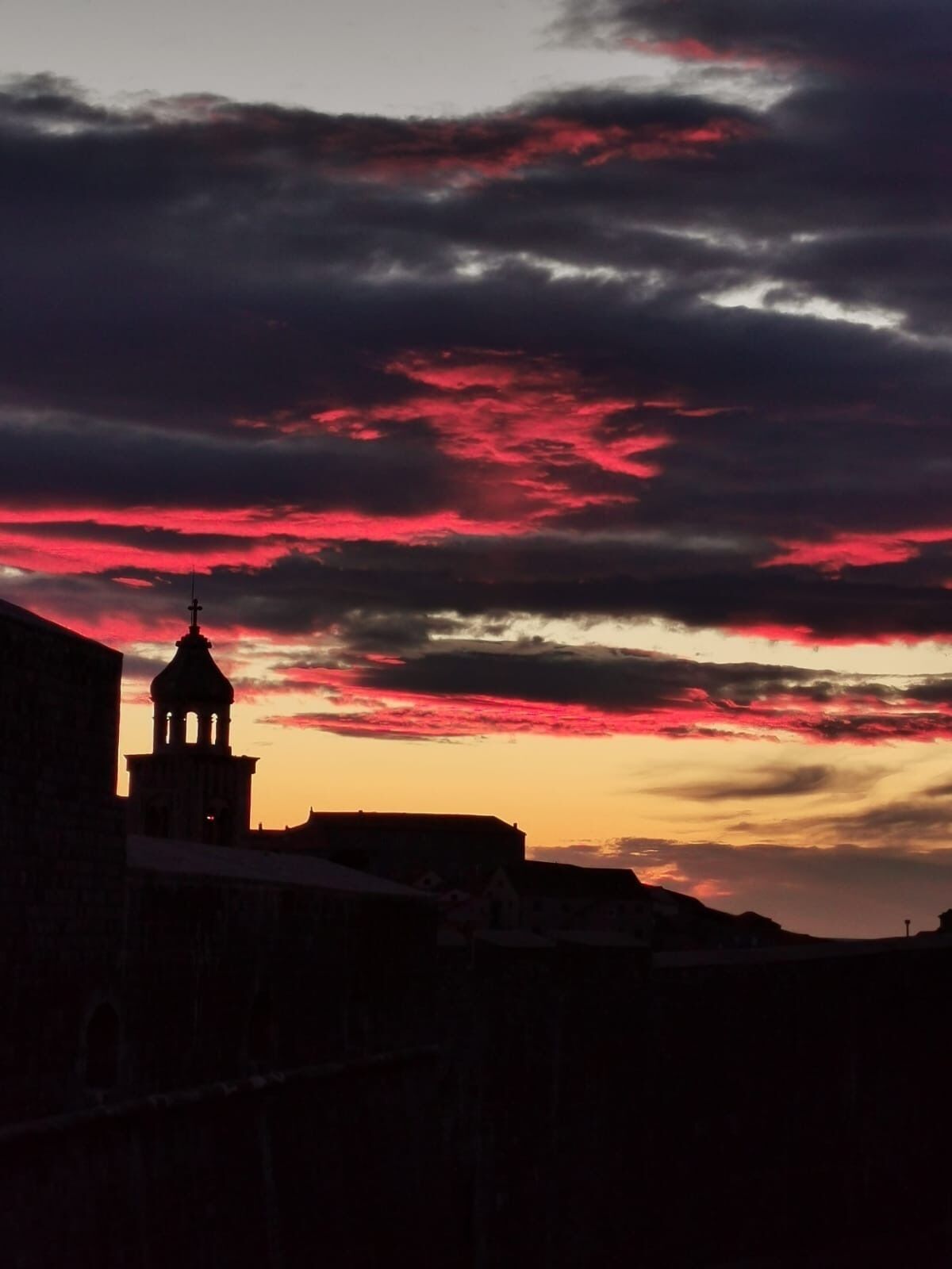 La silhouette d’un bâtiment doté d’un clocher, se découpant sur un ciel crépusculaire aux nuages rouges.