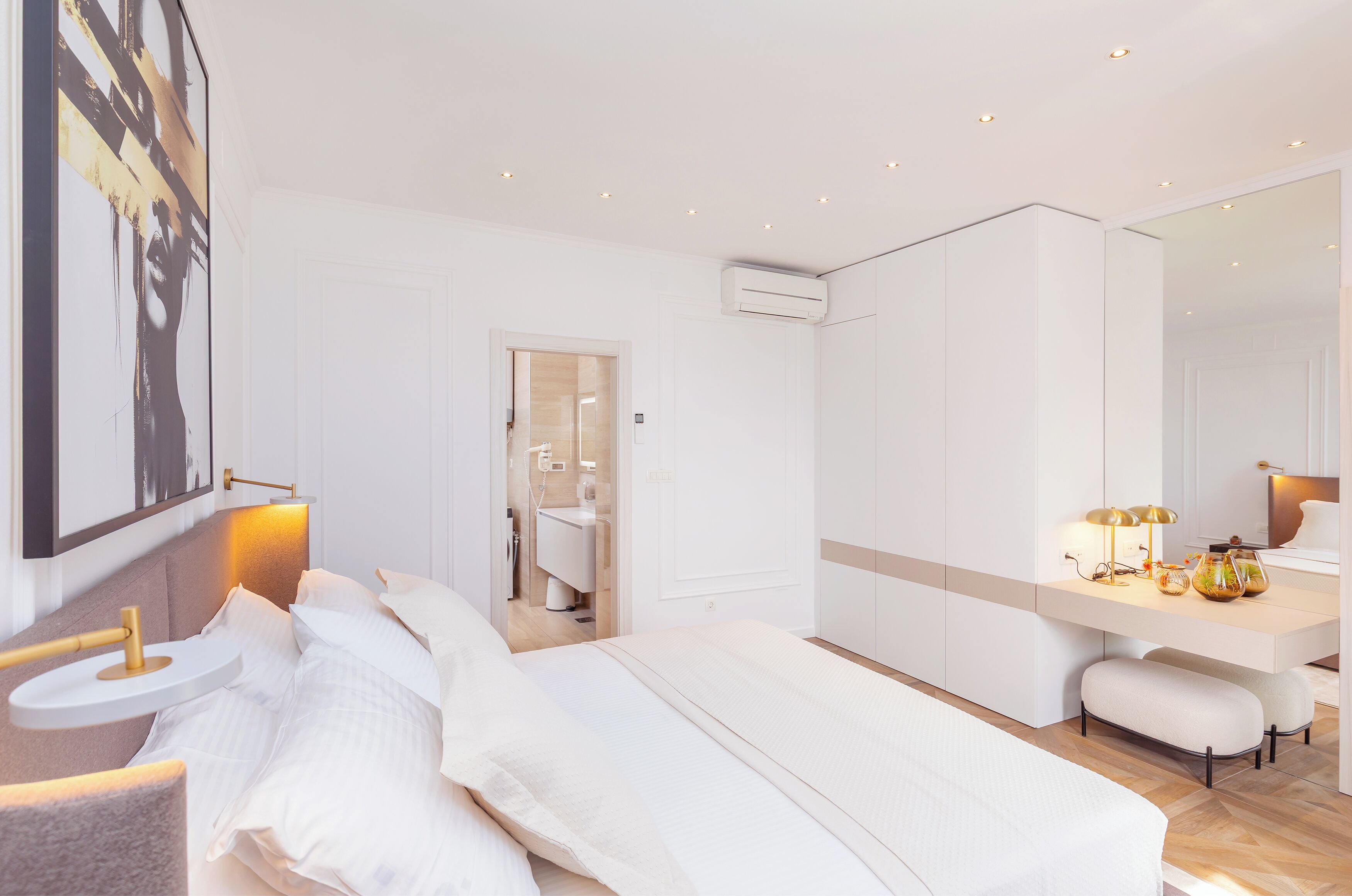 A modern hotel room with a large bed, bedside table, and a desk with a lamp.