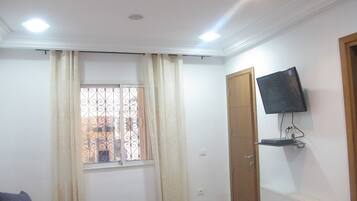 A bedroom with a bed, a TV mounted on the wall, a window with curtains, and a radiator.