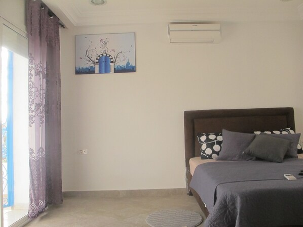 A bedroom with a bed, a window with curtains, a wall-mounted air conditioner, and a painting. - Triplex - Sidi Bou Said (Sidi Bou Said)