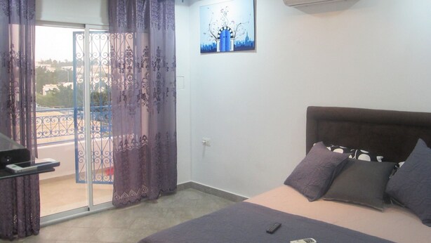 Un dormitorio con cama, escritorio y balcón con cortinas moradas.