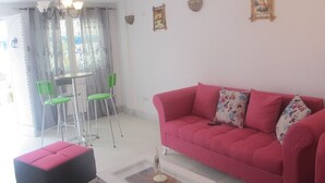 Una sala de estar con un sofá rosa, sillas verdes, una mesa de centro blanca y una araña.