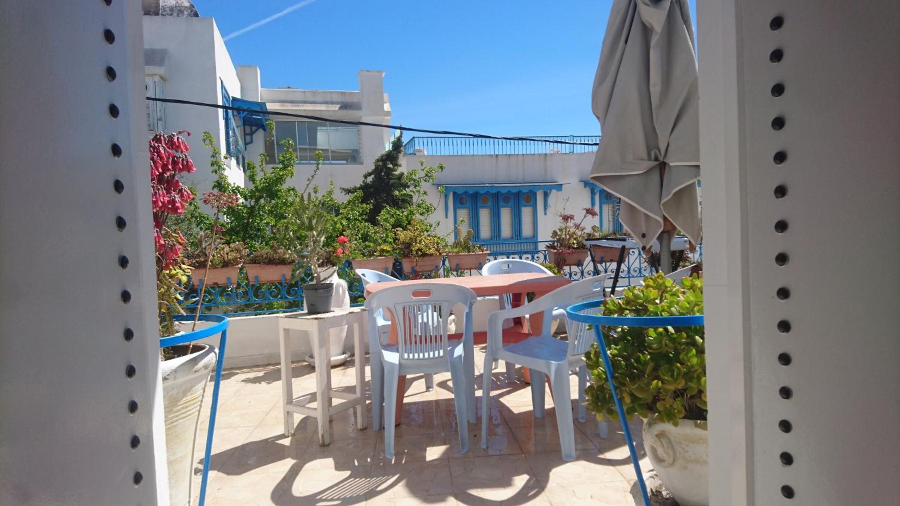 Una terraza con mesa y sillas, plantas en macetas y una barandilla azul.