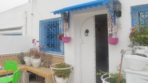 Un edificio blanco con marcos de ventana azules y una puerta, plantas en macetas y una silla verde.