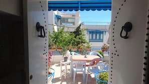 An outdoor seating area with a table and chairs, a potted plant, and a view of a building with blue accents. - Triplex - Sidi Bou Said (Sidi Bou Said)