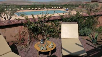 Zona junto a la piscina con sillones, una mesa con tetera y tazas, y vistas a la piscina y el paisaje circundante.