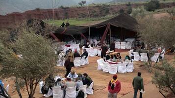 An outdoor event with round tables covered in white tablecloths, surrounded by guests.