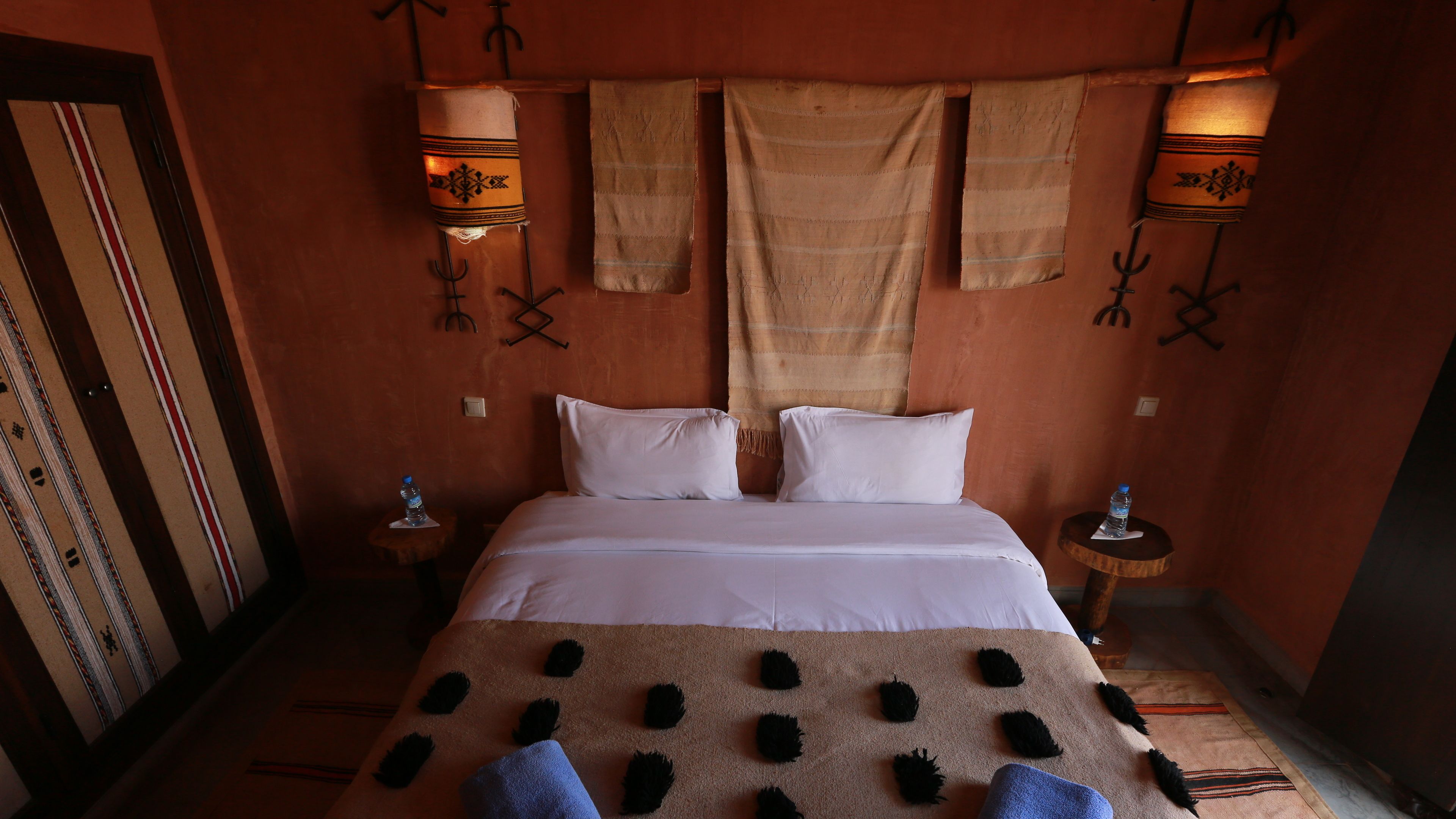A room with a bed, two nightstands, a wall-mounted lamp, and a patterned wall.
