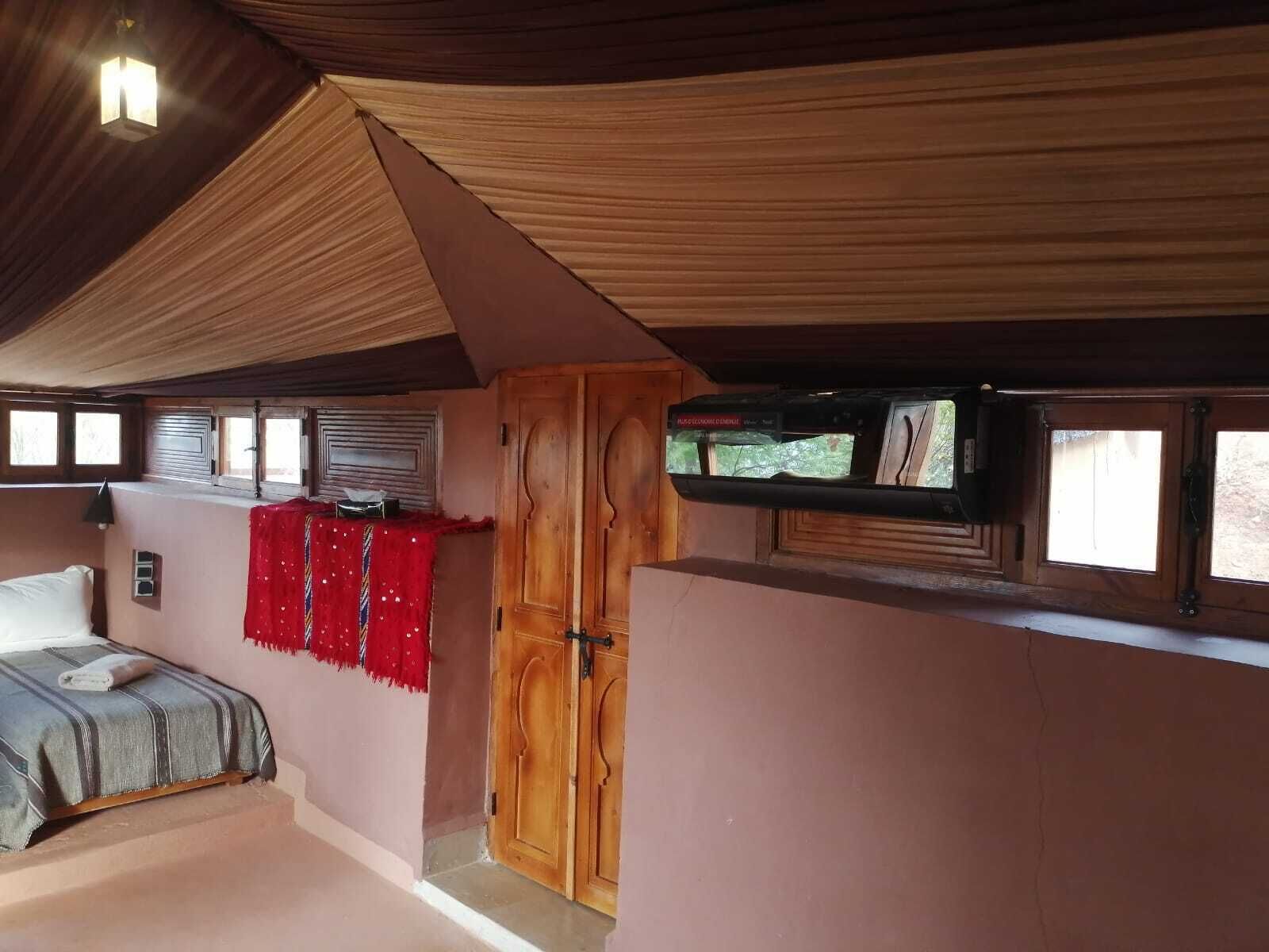A bedroom with a bed, a wooden wardrobe, a television, and a red decorative cloth.