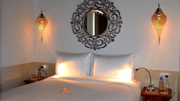 A hotel room with a large bed, two wall-mounted lamps, a decorative mirror, and a bedside table with a bottle and glass. - Riad Dar Dar (Rabat)