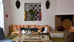 A cozy living area with a sofa, a glass-top table with breakfast items, a decorative wall piece, and a fireplace. - Riad Dar Dar (Rabat)