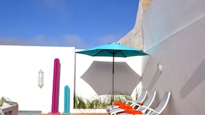 A modern outdoor lounge area with a blue umbrella, white lounge chairs, and decorative pillars. - Riad Dar Dar (Rabat)