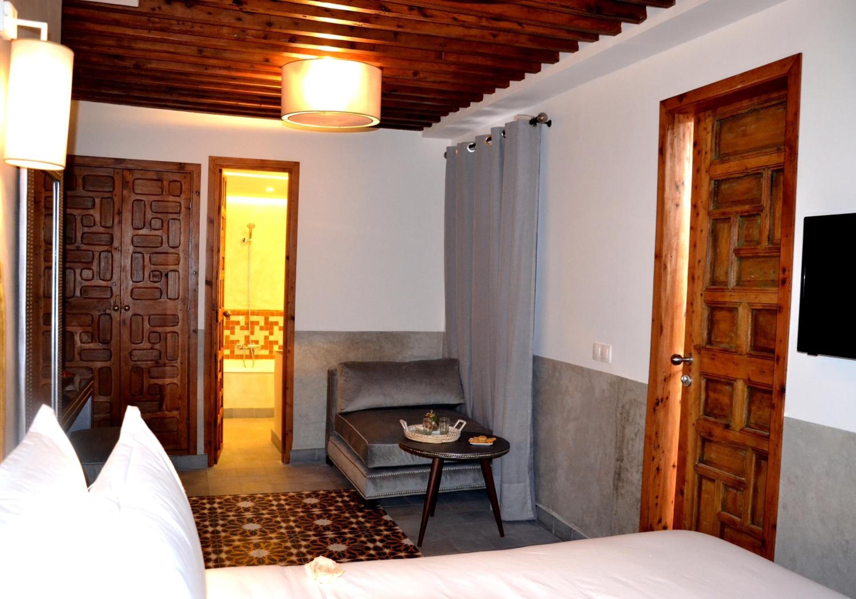 Un dormitorio con cama, sofá, una mesita con bandeja, puerta de madera y zona de ducha.