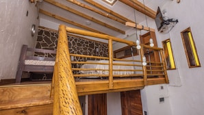 Une chambre mansardée en bois avec un mur en pierre, un escalier en bois et une lucarne.