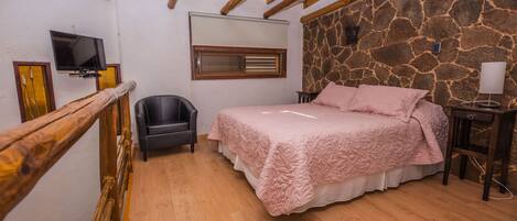 A bedroom with a bed, a chair, a television, and a stone wall.