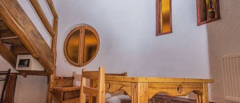 Una habitación rústica con una mesa de madera, sillas, un tapete a rayas y una pared de piedra.