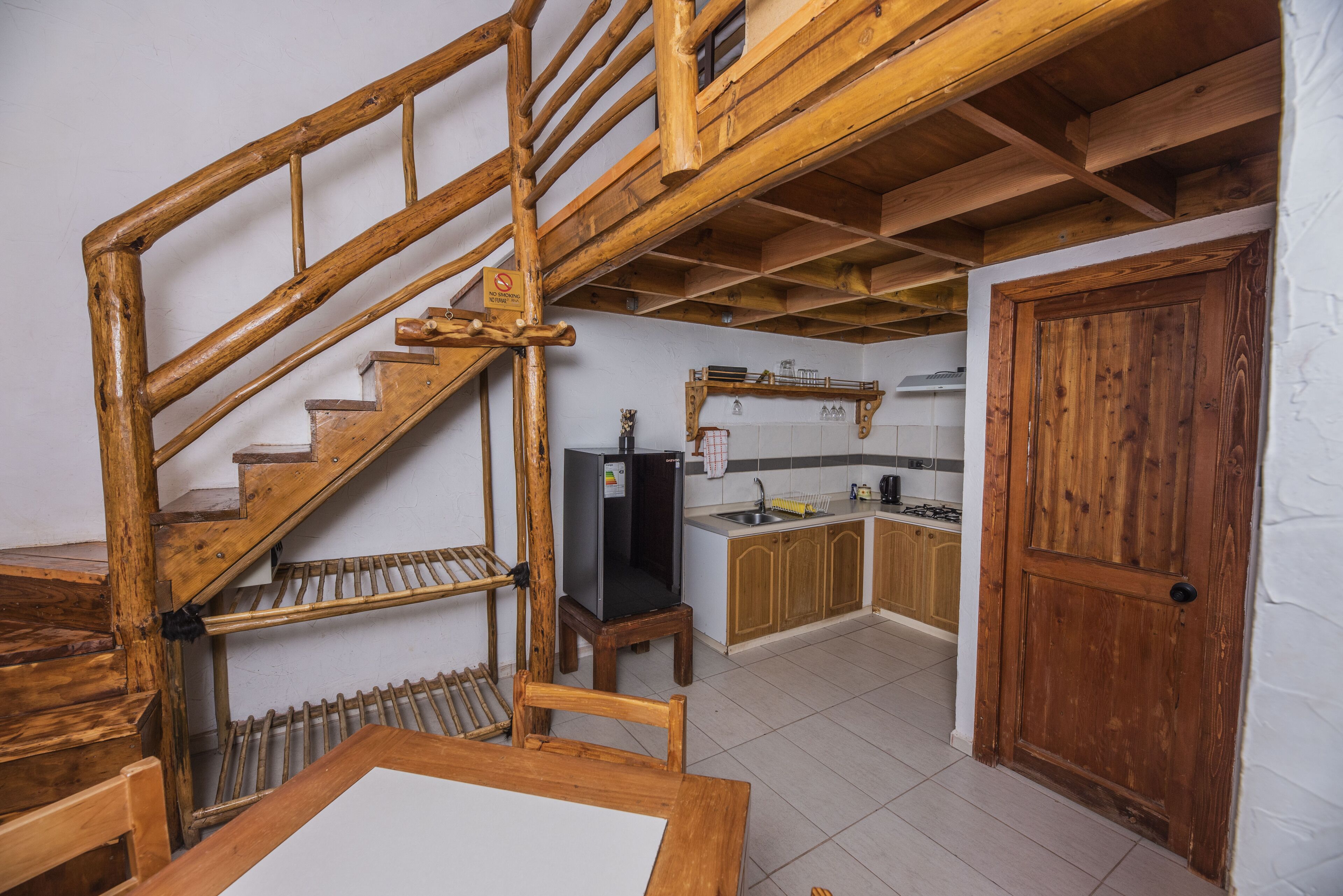 A wooden staircase leading to a kitchen with a refrigerator, sink, and cabinets.