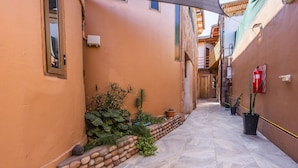 Une ruelle étroite avec un sol carrelé, des plantes en pot et un extincteur fixé au mur.