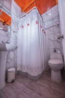 Un baño con cortina de ducha, lavamanos, inodoro y un cubo de basura.