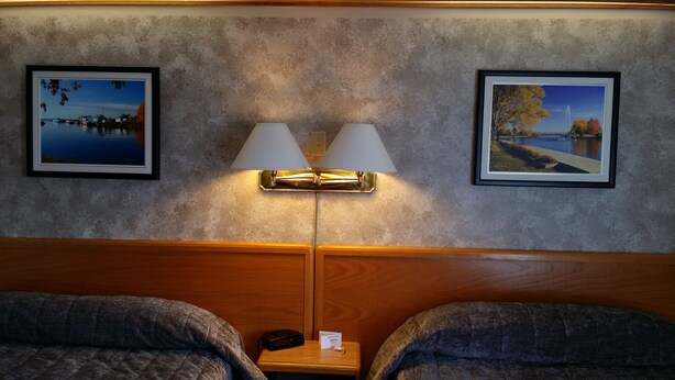 A hotel room with two beds, a nightstand with a lamp, and two framed pictures on the wall.