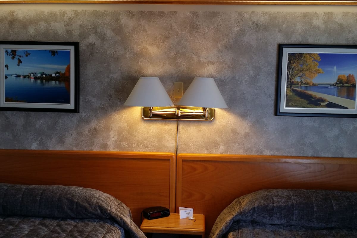 Ein Hotelzimmer mit zwei Betten, einem Nachttisch mit Lampe und zwei gerahmten Bildern an der Wand.