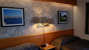 A hotel room with a wooden headboard, two beds, a nightstand with a lamp, and two framed pictures on the wall. - Lakeview Inn (Blind River)