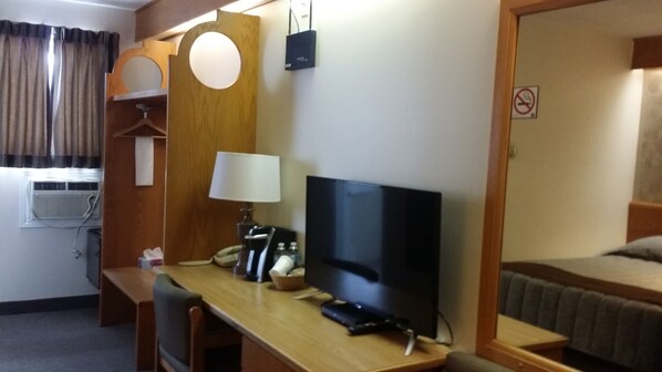 A hotel room with a wooden desk, a television, a lamp, a bed, and a mirror. - Lakeview Inn (Blind River)