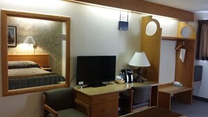 A hotel room with a bed, a desk with a computer, a chair, a TV, a lamp, and a mirror.