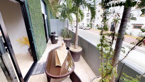 A balcony with a wicker chair, a small table, and potted plants. - Palmares by Playa Moments (Playa del Carmen)
