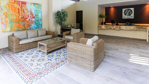 A lobby with wicker furniture, a colorful abstract painting, a reception desk, and a logo on the wall. - Palmares by Playa Moments (Playa del Carmen)