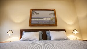 A neatly made bed with a striped bedspread and two pillows, a framed picture of a beach scene on the wall, and two bedside lamps. - Plaza Marbella Granada Condiminiums (Granada)
