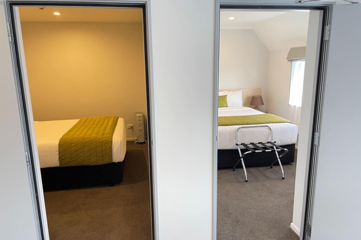 A hotel room with two beds, a small table, and a chair.