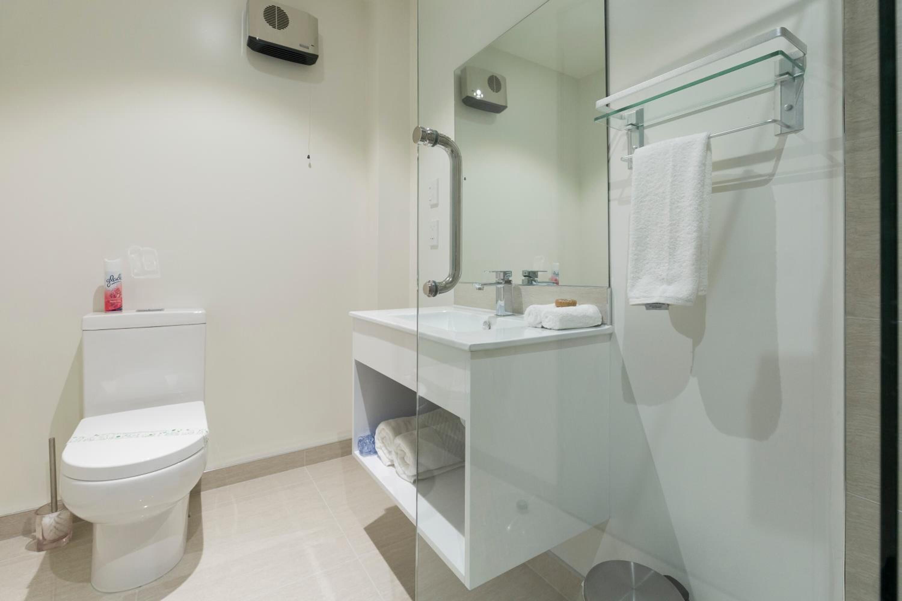Un baño moderno con inodoro, cabina de ducha con mampara de vidrio y lavamanos con superficie de vidrio y toallero.