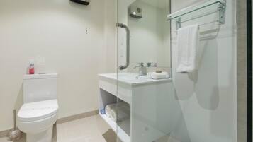 Un baño moderno con inodoro, cabina de ducha con mampara de vidrio y lavamanos con superficie de vidrio y toallero.