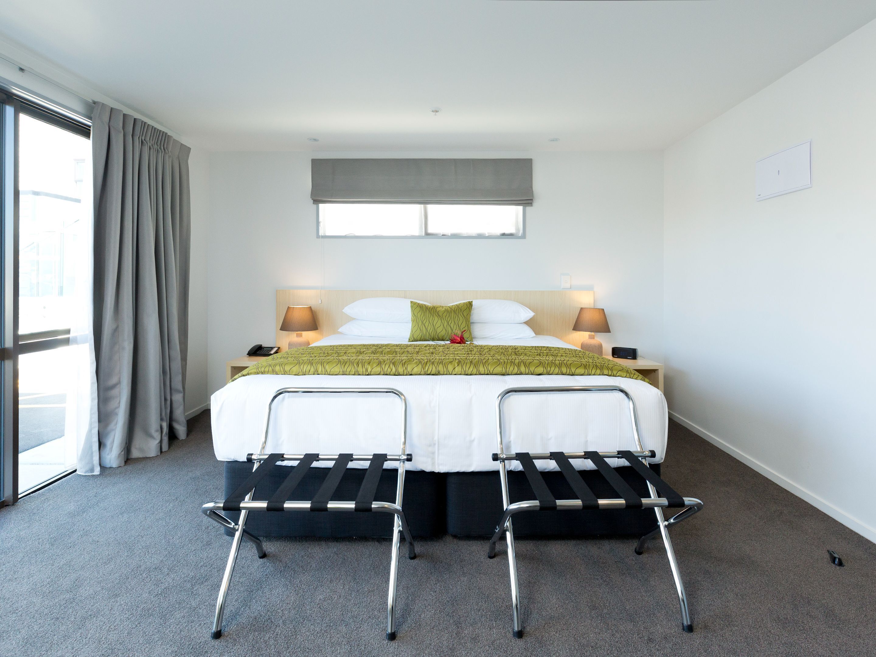 A hotel room with a bed, two bedside tables, a window with curtains, and a chair with a tray.