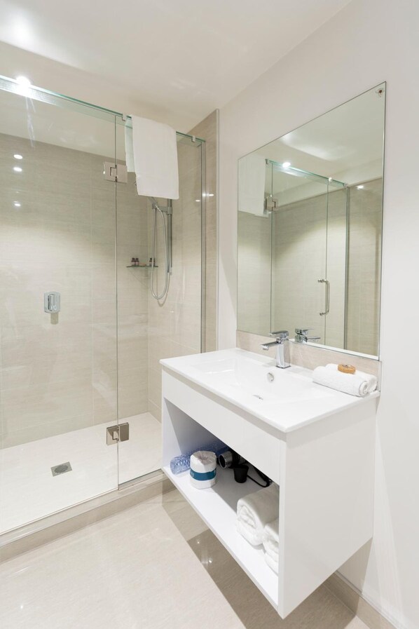 A modern bathroom with a glass shower enclosure, a white vanity with a mirror, and a built-in shelf for toiletries.