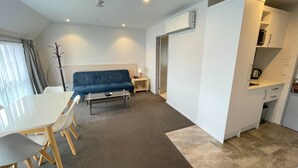 Una sala de estar moderna con un sofá azul, una mesa de comedor con sillas, una mesa de centro y una zona de cocina con microondas y armarios.