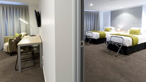 Habitación de hotel con dos camas, un escritorio, una silla, televisión y ventana con cortinas.