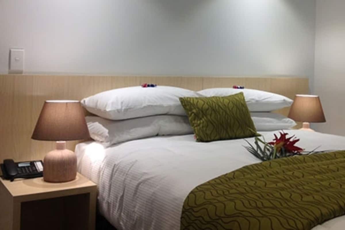 A hotel room with a bed, two bedside lamps, a telephone, and a green throw blanket.