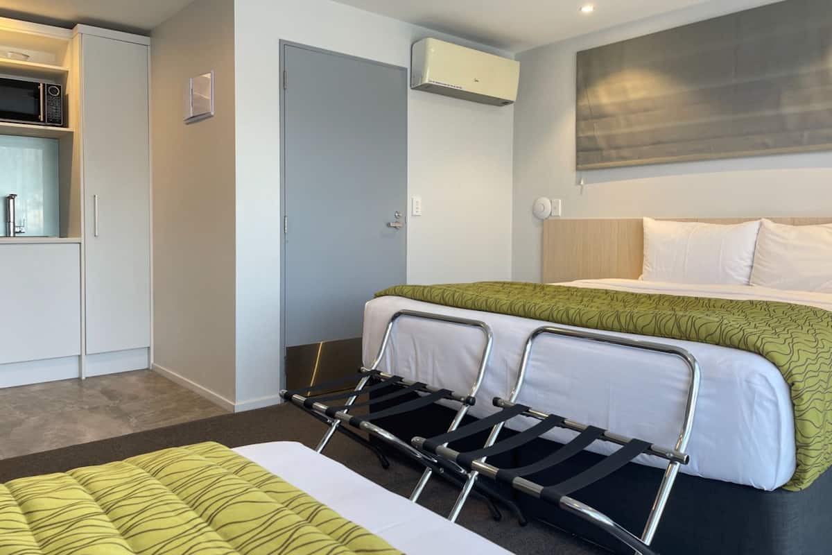 A hotel room with a bed, a small kitchenette, a door, and an air conditioning unit.