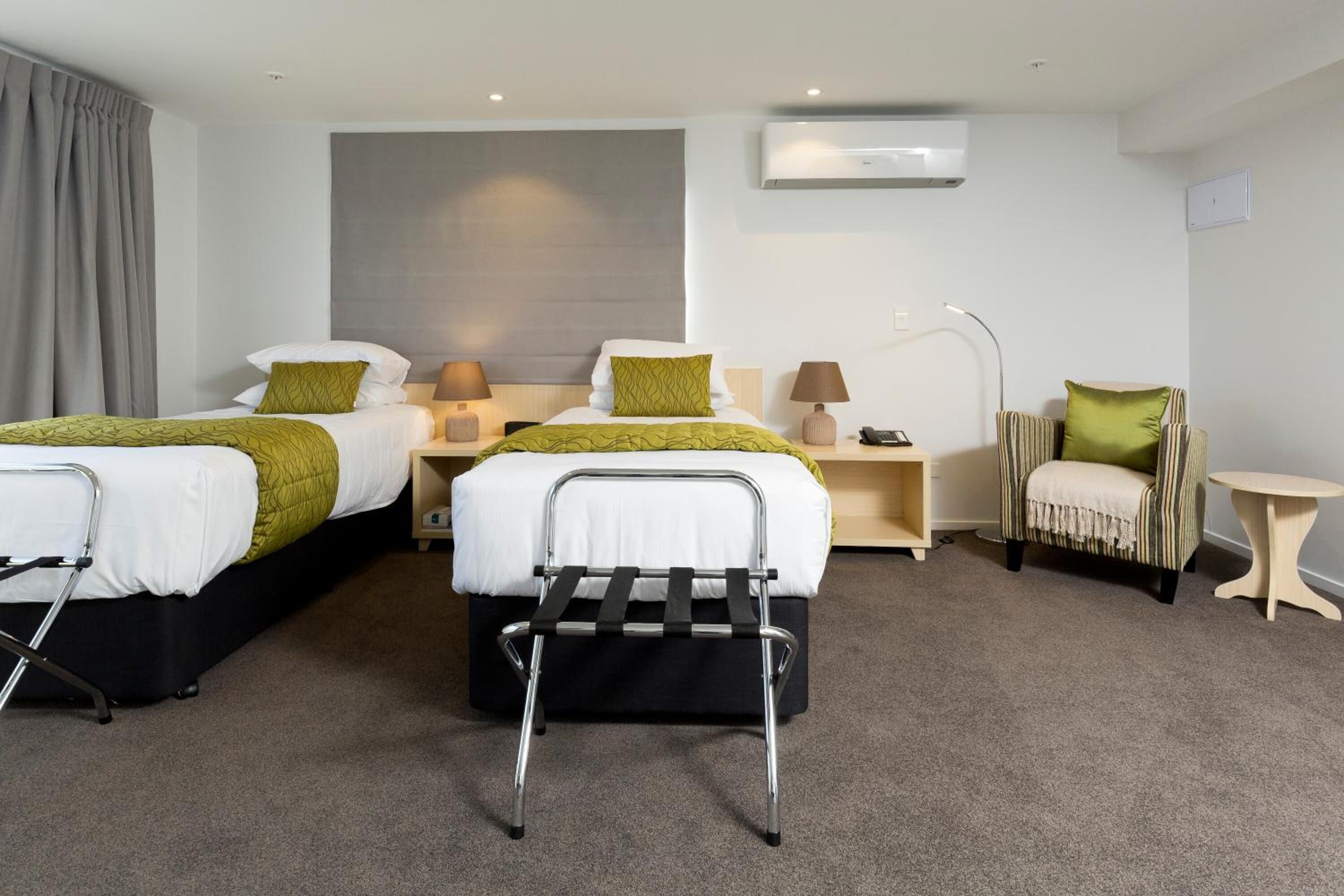 Une chambre d’hôtel avec deux lits, une table de chevet avec des lampes, une chaise, une petite table et un climatiseur fixé au mur.